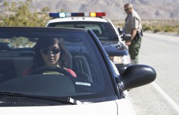 A woman with a traffic ticket sitting in car pulled over by a police officer.