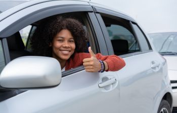 Happy Afro-American woman driver sitting in a car and showing her thumb up.