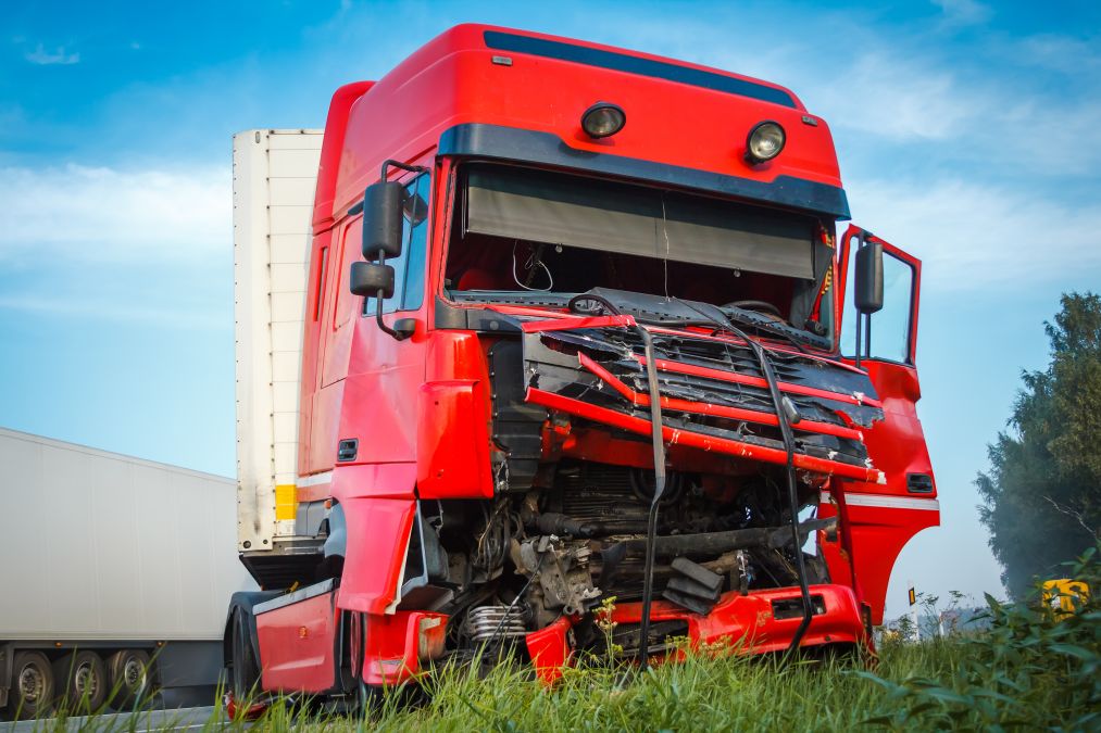 A heavily damaged red semi-truck involved in a wreck, resting on a grassy roadside under a blue sky—a visual representation of why victims seek a truck accident lawyer in Tampa, FL.